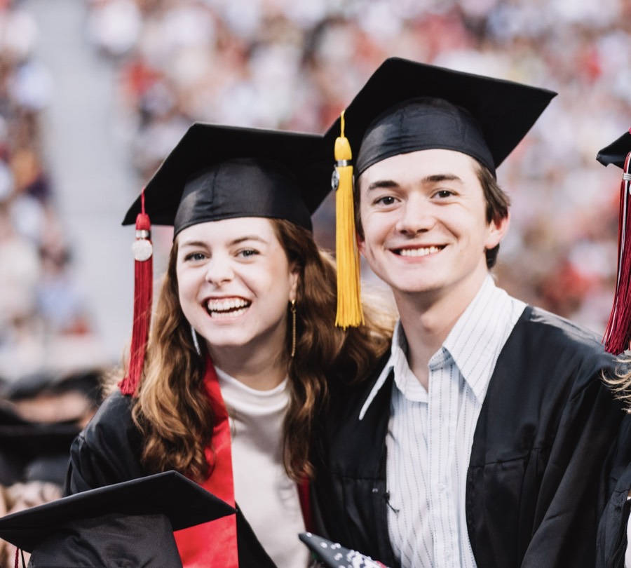 Elizabeth and Nicholas holding up their decorated graduation caps.