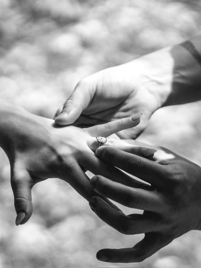 Nicholas sliding the engagement ring onto Elizabeth’s finger, in black and white.